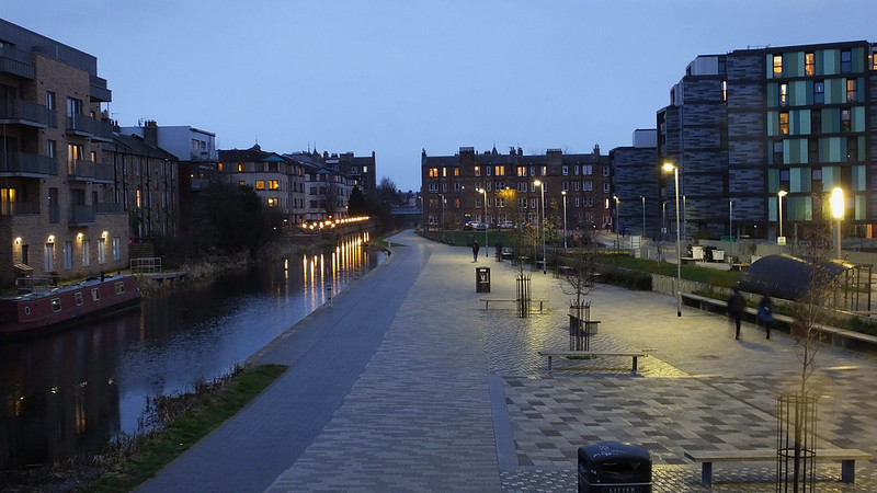 A photo of Fountainbridge canal at night, streetlights softly light up the canal path with a range of flats in the background.